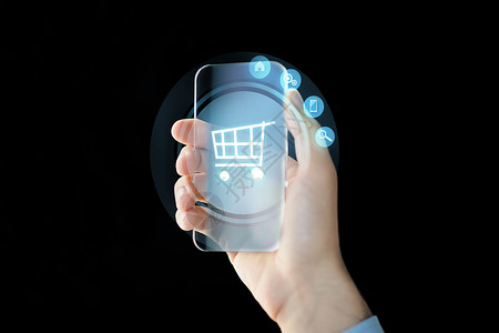 手托购物车图标商业,未来的技术人的近距离的男手握透明的智能手机与购物车图标屏幕上的黑色背景背景