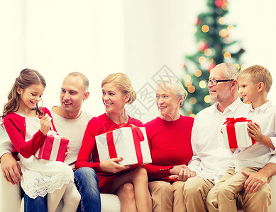 家庭,假日,世代人的微笑的家庭与礼品盒坐沙发上的客厅与诞树背景图片