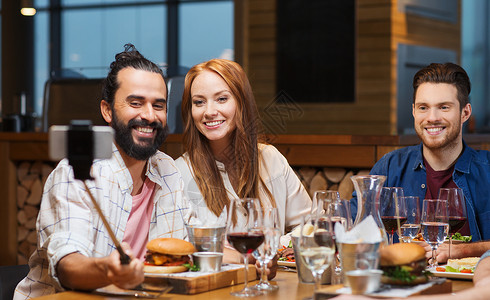 休闲,技术,友谊,人假日的快乐的朋友餐厅用智能手机自拍棒吃饭拍照图片