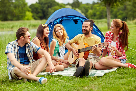 野餐人们的朋友带着帐篷饮料,露营时弹吉他背景图片