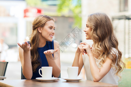 令人愉快的喝人,沟通友谊的微笑的轻妇女喝咖啡茶,户外咖啡馆交谈背景