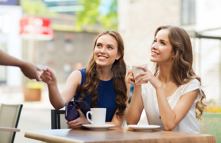 人,消费主义,生活方式友谊的微笑的轻妇女给服务员的手信用卡支付咖啡户外咖啡馆图片