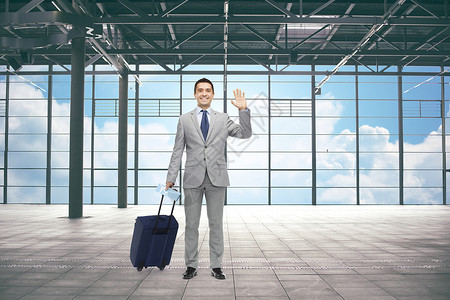 商务旅行,旅游,手势人的穿着旅行袋的快乐商人挥舞着机场航站楼的背景图片