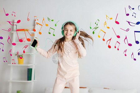 孩子听音乐人们,孩子,睡衣派技术快乐的微笑女孩戴着耳机,用智能手机床上跳跃,家听音乐背景
