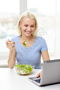 健康的饮食,饮食,食物,技术人的微笑的轻女人带着笔记本电脑家吃蔬菜沙拉图片