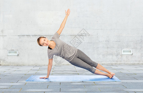健身,运动,人健康的生活方式妇女瑜伽侧木板姿势垫子上的城市街道背景图片