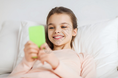 人,孩子,休息技术快乐的微笑女孩躺家里的床上,用智能手机睡着图片