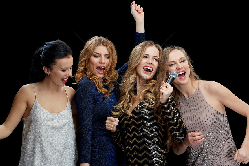 假期,朋友,单身派,夜生活人的三个女人穿着晚礼服,戴着麦克风黑色背景下唱卡拉OK图片
