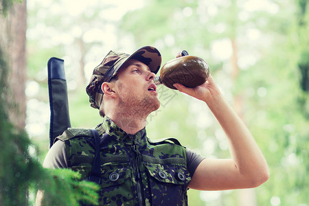 士兵烧瓶徒步旅行,轻的士兵护林员用森林里的烧瓶里喝背景