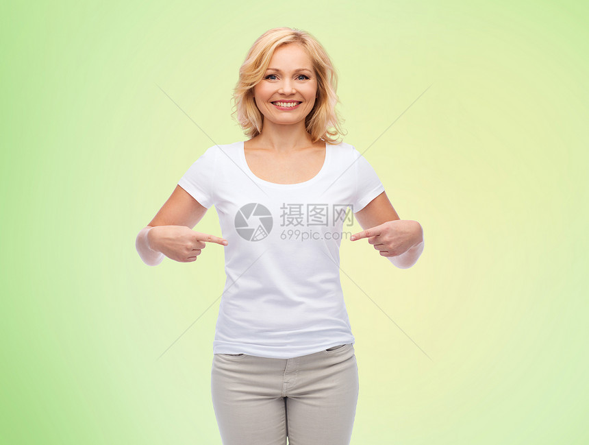 手势,广告人的微笑的中妇女,穿着空白的白色t恤,绿色的自然背景上指着自己图片