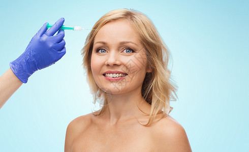 美容,抗衰容手术的微笑的女人脸美容师携手手套与注射器,注射额头蓝色背景图片