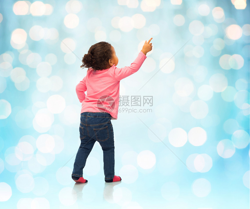 人,种族,种族童的快乐的非裔美国女婴指指点点的东西背后蓝色假日灯光背景图片