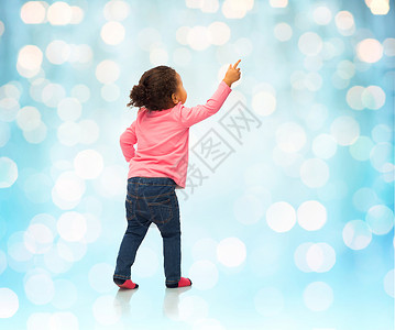 人,种族,种族童的快乐的非裔美国女婴指指点点的东西背后蓝色假日灯光背景图片