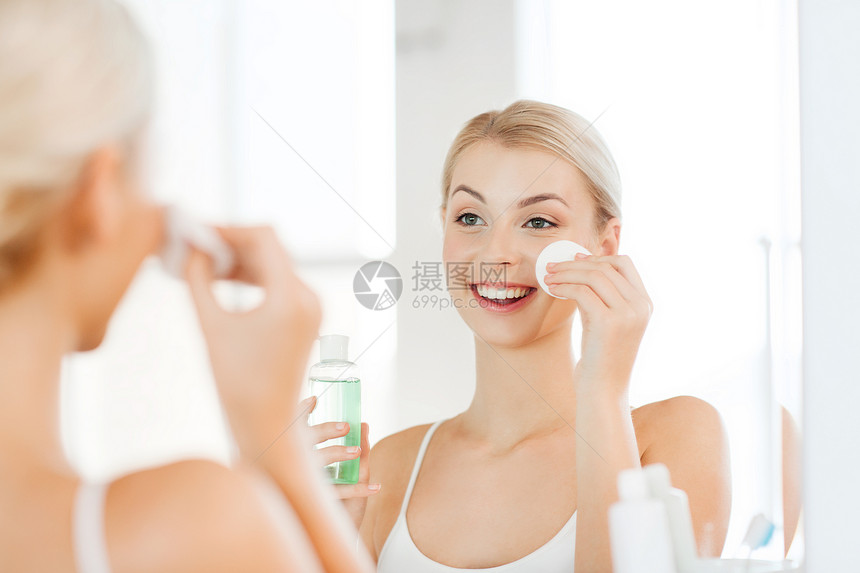 美丽,皮肤护理人的微笑的轻妇女应用乳液棉花盘,以洗她的脸浴室图片
