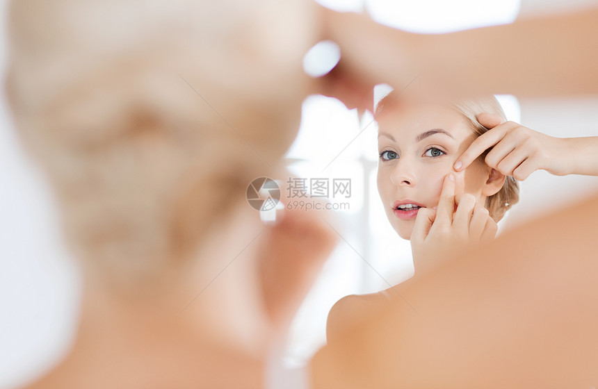 美容,卫生,皮肤问题人的轻的女人看着镜子挤压粉刺家里的浴室图片