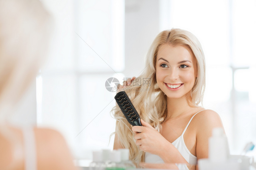 美丽,修饰人的微笑的轻女人看着镜子,家里的浴室用梳子梳头图片