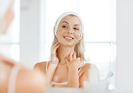 美丽,皮肤护理人的微笑的轻女人发带触摸她的脸镜子家里的浴室图片