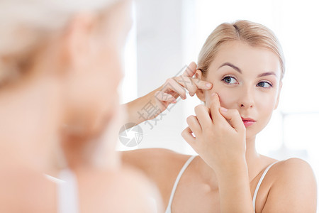 美容,卫生,皮肤问题人的轻的女人看着镜子挤压粉刺家里的浴室背景图片