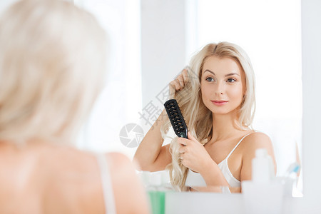 美容,护发人的微笑的轻女人看着镜子,家里的浴室用梳子刷头发图片