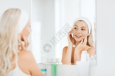 美丽,皮肤护理人的微笑的轻女人发带触摸她的脸镜子家里的浴室背景图片