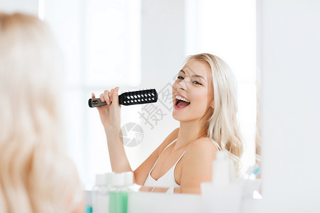 美容,护发人的微笑的轻女人看着镜子,唱歌,家里的浴室刷毛梳子图片