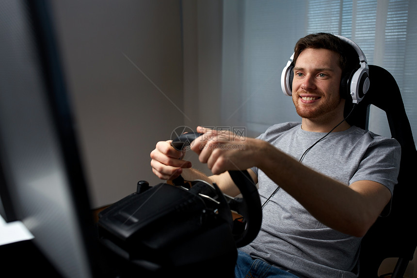 技术,游戏,娱乐活动人的快乐的微笑轻人耳机与个人电脑玩赛车电子游戏家里方向盘图片