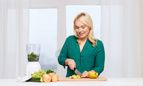 健康的饮食,烹饪,素食,饮食人的微笑的轻妇女与搅拌机刀切水果蔬菜切割板家里图片