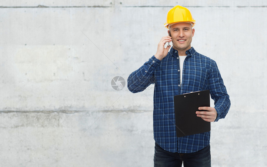 维修,建筑,商业维修微笑的人建筑工人头盔与剪贴板调用智能手机灰色混凝土墙背景图片