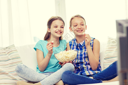 人,孩子,电视,朋友友谊的两个快乐的小女孩电视上看喜剧电影,家吃爆米花图片
