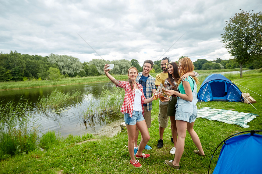 野营,旅游,远足人们的快乐的朋友用璃瓶喝苹果酒啤酒,并露营时用智能手机自拍图片