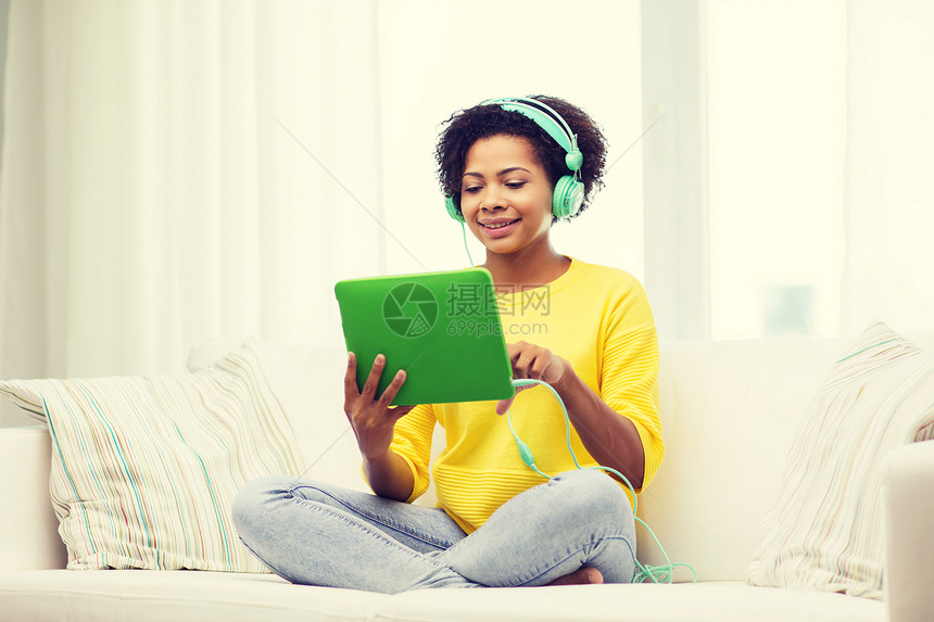 人,技术休闲快乐的非裔美国轻妇女坐沙发上,用平板电脑耳机家听音乐图片