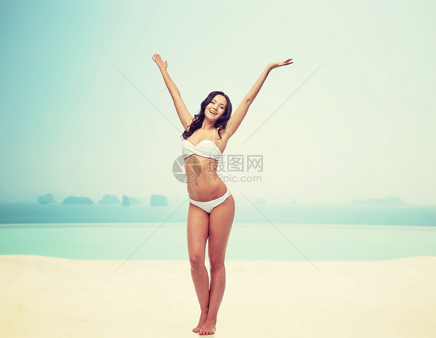 人们,时尚,泳装,夏天海滩的快乐的轻女人穿着白色比基尼泳衣,举手海滩度假胜地的无限游泳池上跳舞图片