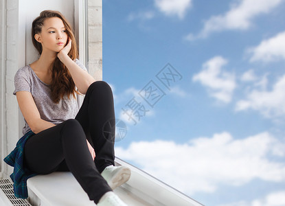 人,情感青少的悲伤,快乐,漂亮的十几岁女孩坐窗台上,透过窗户看蓝天云彩的背景图片