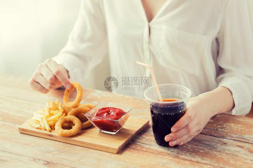 快餐,人健康的饮食观念密切妇女吃油炸鱿鱼戒指,炸薯条与番茄酱饮用可乐木桌上图片