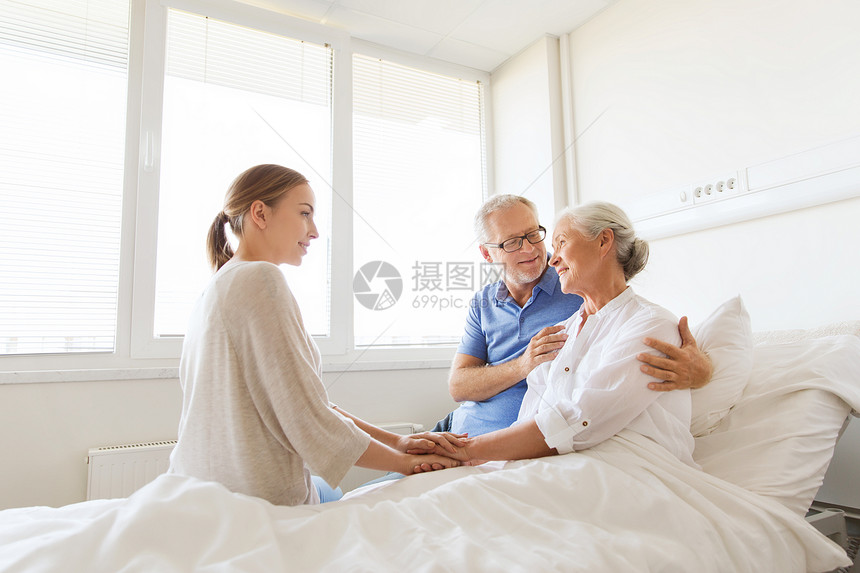 医学,支持,家庭保健人的快乐的老人轻的女人拜访欢呼她的祖母躺医院病房的床上图片
