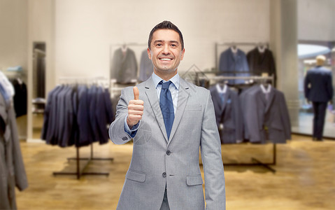 商业,人,男装,销售服装快乐的微笑商人穿着西装,服装店的背景上竖大拇指图片