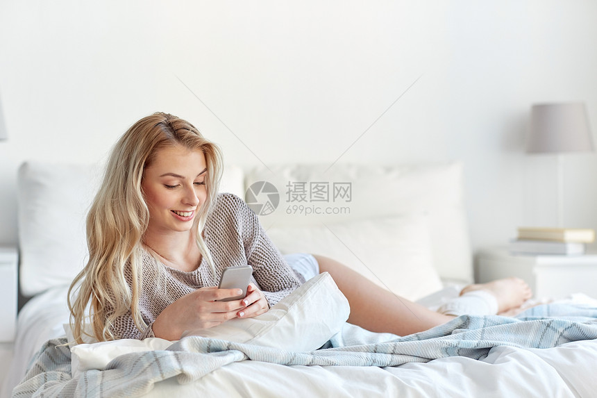 技术,沟通人的快乐的轻女人躺床上,家里的卧室用智能手机发短信图片