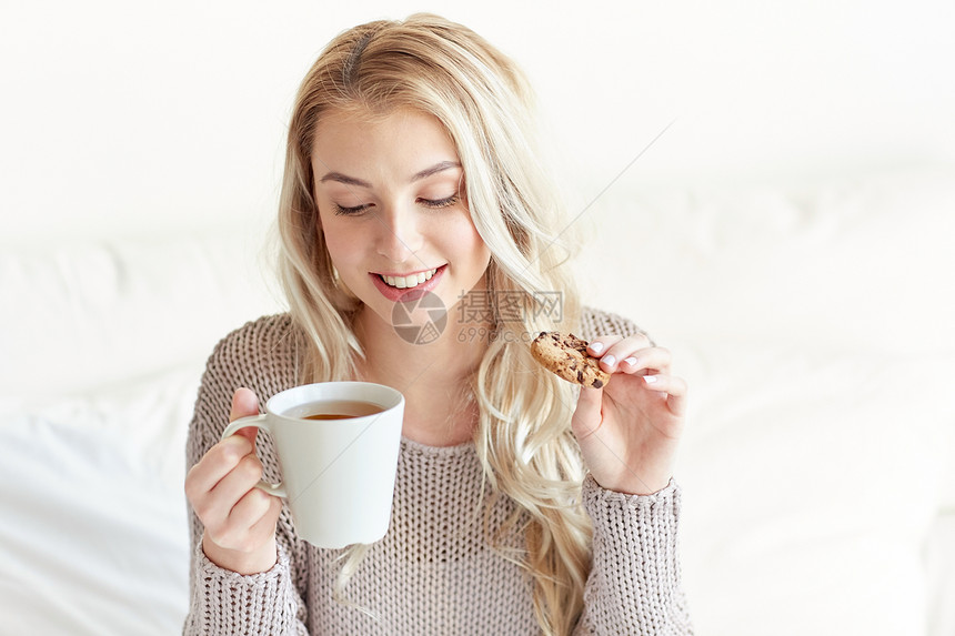 早上,休闲人们的快乐的轻女人家里卧室的床上喝着茶吃饼干图片