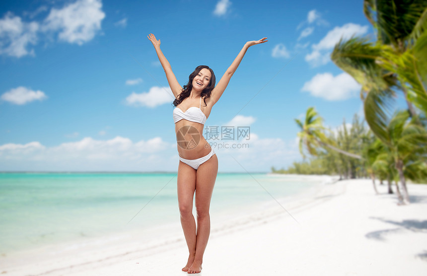 人们,泳装,旅游,暑假海洋快乐的轻女人穿着白色比基尼泳衣,热带海滩背景上摆姿势举手跳舞图片