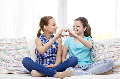 人,孩子,朋友友谊的快乐的小女孩坐沙发上,家里展示心形的手牌图片