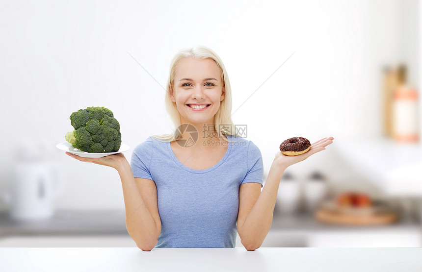 健康饮食,垃圾食品,饮食选择人的微笑的女人选择西兰花甜甜圈厨房背景图片