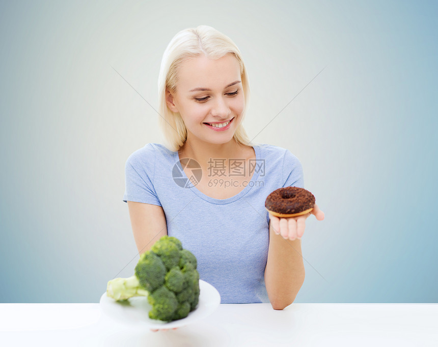 健康饮食,垃圾食品,饮食选择人的微笑的女人选择西兰花甜甜圈蓝色背景图片
