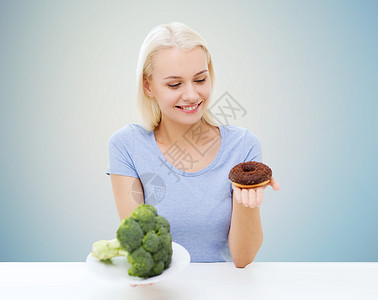 健康饮食,垃圾食品,饮食选择人的微笑的女人选择西兰花甜甜圈蓝色背景图片