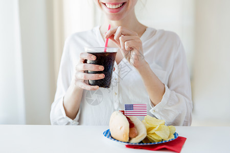 国防灾减灾日美国独立日,庆祝,主义节日的快乐的女人喝可口可乐塑料杯与热狗薯片7月4日的家庭聚会背景