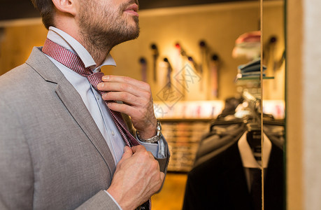 销售,购物,时尚,风格人的接近轻人穿着西装,选择捆绑领带,并商场服装店照镜子背景图片
