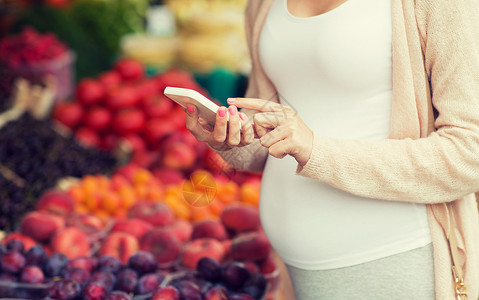 智能市场销售,购物,食物,怀孕人们的孕妇与智能手机街头市场背景