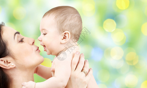 家庭,母亲,养育,人儿童保育的快乐的母亲亲吻可爱的婴儿绿色假日灯光背景图片