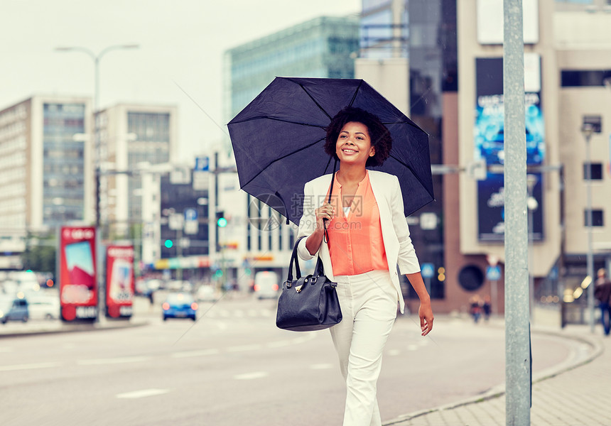 商业人的轻微笑的非裔美国女商人带着雨伞手提包走城市街道上快乐的非裔美国女商人带着雨伞图片
