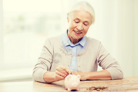 之内储蓄,金钱,金保险,退休人们的微笑的老年女子家里把硬币放进储蓄罐背景