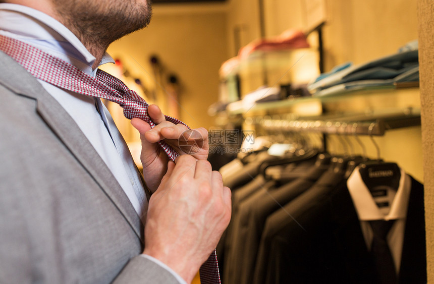 销售,购物,时尚,风格人的接近轻人穿着西装,选择捆绑领带,并商场服装店照镜子图片